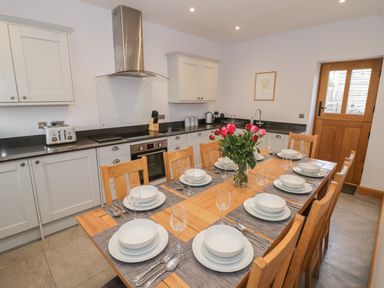 A kitchen with dining table set for eight and flowers on the table at The Stables in Droitwich Spa