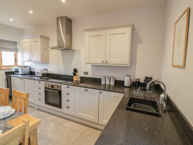 A kitchen with wooden chairs a dining table white cabinets black countertops and stainless steel appliances at The Stables in Droitwich Spa