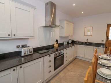 A kitchen with white cabinets black countertops a toaster stove oven knife block and a dining table with plates and glasses at The Stables in Droitwich Spa
