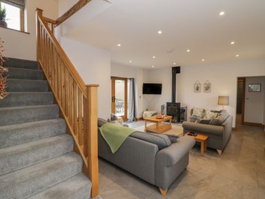 A living room with grey sofas, wooden coffee tables, a wood stove, and carpeted stairs at The Stables in Droitwich Spa