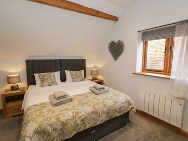 A bedroom with a double bed two nightstands lamps towels on bed window and heart decoration on wall at The Stables in Droitwich Spa