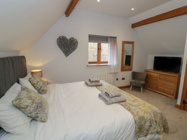 A bedroom with a bed pillows towels a lamp heart wall decoration window mirror chair dresser and TV at The Stables in Droitwich Spa