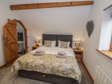 A bedroom with a bed two bedside tables with lamps a wooden door to a bathroom and a heart-shaped wall decoration at The Stables in Droitwich Spa