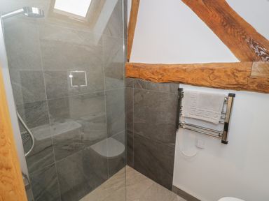 A bathroom shower area with gray tiles wooden beams and a towel rack at The Stables in Droitwich Spa