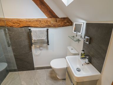 A bathroom with a toilet sink mirror towel rack and wooden beam at The Stables in Droitwich Spa
