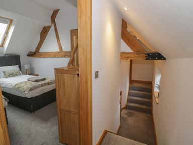 A bedroom with a bed and a wooden cabinet next to a hallway with stairs and exposed wooden beams at The Stables in Droitwich Spa
