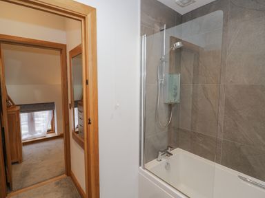 A bathroom with a bathtub and shower next to a hallway leading to a carpeted room at The Stables in Droitwich Spa