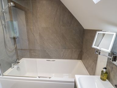 A bathroom with a bathtub shower combination with tiled walls and a mirror with light at The Stables in Droitwich Spa