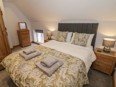 A bedroom with a double bed with patterned bedding and towels on it wooden furniture and lamps on bedside tables at The Stables in Droitwich Spa