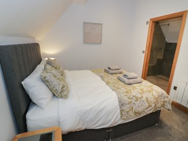 A bedroom with a bed with pillows and folded towels and an open door to a bathroom at The Stables in Droitwich Spa