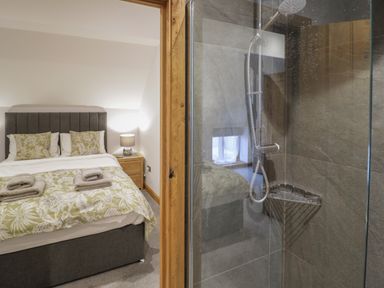 A bedroom with a bed and bedside table next to a shower with glass walls at The Stables in Droitwich Spa