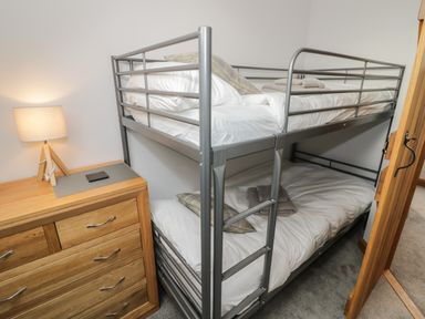 A metal bunk bed with white bedding and folded towels next to a wooden chest of drawers with a lamp at The Stables in Droitwich Spa