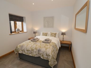 A bedroom with a bed with floral bedspread two bedside tables lamps window with blind and a wall mirror at The Stables in Droitwich Spa