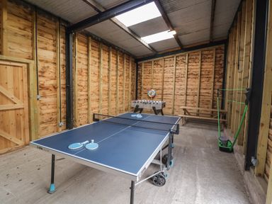 An indoor recreational space with a ping pong table foosball table bench and shuttlecock set up at The Stables in Droitwich Spa