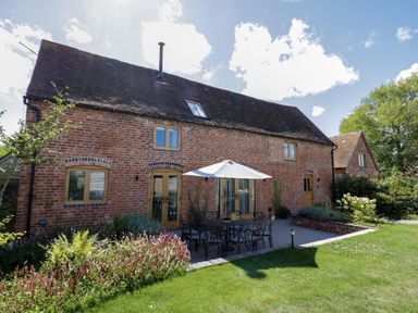 A brick house with wooden windows and doors a patio with a table umbrellas and chairs and a garden at The Stables in Droitwich Spa