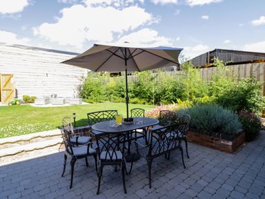 A garden patio with metal table and chairs under an umbrella and plants in raised beds at The Stables in Droitwich Spa