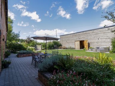 A garden with outdoor furniture tables chairs and umbrella next to a large wooden barn at The Stables in Droitwich Spa