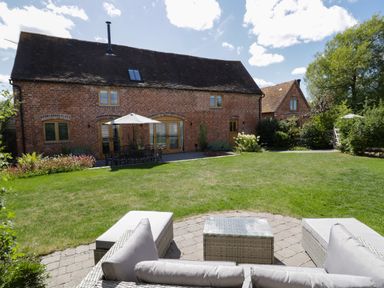 A backyard with lawn seating and table with umbrella outside a brick house at The Stables in Droitwich Spa