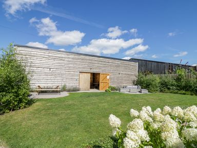 An outdoor garden area with green grass a wooden bench a sofa set and a wooden barn building at The Stables in Droitwich Spa