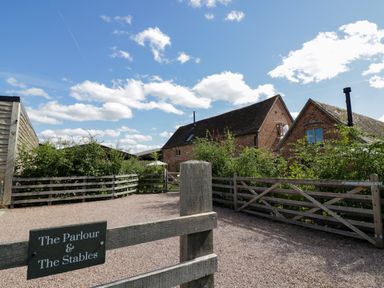 A gravel driveway with wooden fences and two brick buildings under a blue sky at The Stables in Droitwich Spa