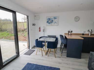 A dining area with a glass table and four blue chairs beside a kitchen counter with two bar stools at Goldthorne Lodge in Clee Hill