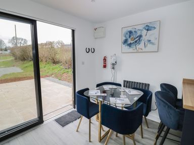 A dining area with a glass table and blue chairs next to sliding glass doors at Goldthorne Lodge in Clee Hill