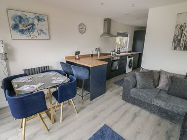 A kitchen and dining room with blue chairs a glass table and gray sofa at Goldthorne Lodge in Clee Hill