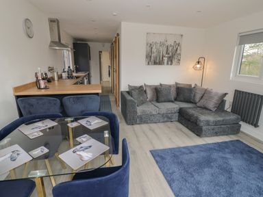 A living room with a grey sectional sofa a blue rug and a glass dining table with blue chairs at Goldthorne Lodge in Clee Hill