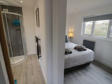 A bedroom with a bed and folded towels next to an en suite shower room with a glass door at Goldthorne Lodge in Clee Hill