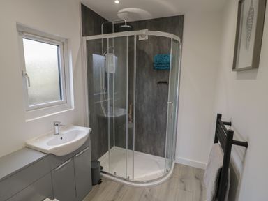 A bathroom with a glass shower enclosure a sink with a cabinet a window and a towel rail at Goldthorne Lodge in Clee Hill