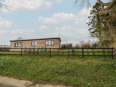 A wooden single-story building with windows behind a black fence and green grass at Goldthorne Lodge in Clee Hill