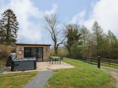 An outdoor patio with a hot tub and metal table with chairs next to a wooden cabin at Goldthorne Lodge in Clee Hill