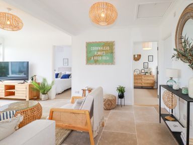 A living room with wooden furniture and plants with bedrooms visible through doorways at Polwen in Harlyn Bay Padstow
