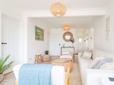A living room with white furniture a woven coffee table and wall art at Polwen in Harlyn Bay Padstow