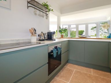 A kitchen with green cabinets a built-in oven and utensils on the counter at Polwen in Harlyn Bay Padstow