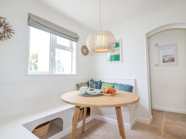 A breakfast nook with a round wooden table cushions on bench seating and a hanging light at Polwen in Harlyn Bay Padstow