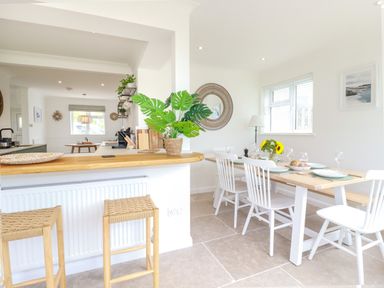 A dining area with a wooden table set with plates and glasses beside a kitchen counter with two stools at Polwen in Harlyn Bay Padstow
