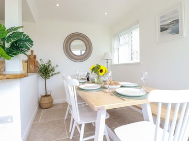 A dining room with a wooden table set with plates glasses and a vase with sunflowers at Polwen in Harlyn Bay Padstow