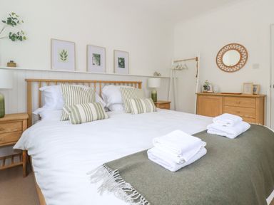 A bedroom with a double bed with white linens and green striped pillows at Polwen in Harlyn Bay Padstow