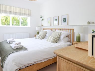 A bedroom with a wooden bed frame white bedding and green striped pillows at Polwen in Harlyn Bay Padstow
