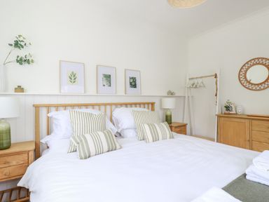 A bedroom with a wooden bed frame striped pillows nightstands and framed art at Polwen in Harlyn Bay Padstow