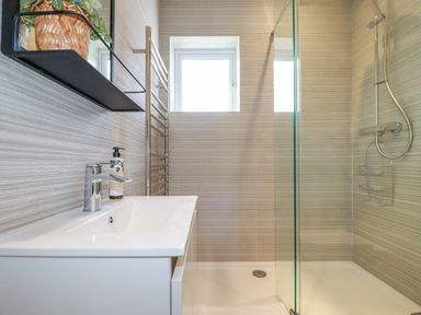 A bathroom with a sink soap dispenser mirror plant towel rack shower area and window at Polwen in Harlyn Bay Padstow