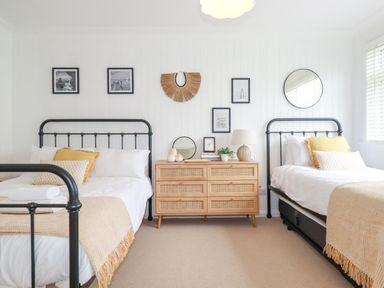 A bedroom with two metal frame beds and a wooden dresser with decorations at Polwen in Harlyn Bay Padstow