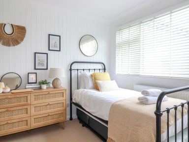 A bedroom with a single bed a wooden dresser with a lamp framed pictures and a round mirror at Polwen in Harlyn Bay Padstow