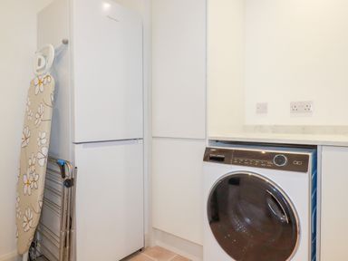 A utility room with a washing machine fridge ironing board and drying rack at Polwen in Harlyn Bay Padstow