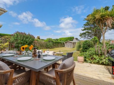An outdoor dining table with chairs and tableware on a wooden deck in a garden at Polwen Harlyn Bay Padstow