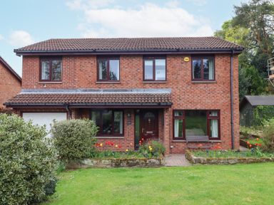 A two story brick house with a tiled roof and a front garden with flowers and bushes at Sparrow House in Alnwick