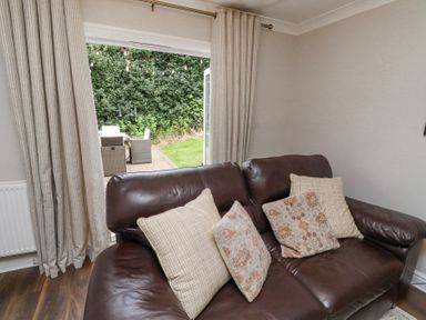 A brown leather sofa with four cushions in a living room with open curtains showing an outdoor patio at Sparrow House in Alnwick
