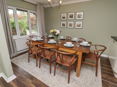 A dining room with a wooden table set with plates bowls glasses and flowers on a rug by a window at Sparrow House in Alnwick