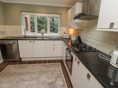 A kitchen with white cabinets black countertops a gas stove a dishwasher and a window at Sparrow House in Alnwick